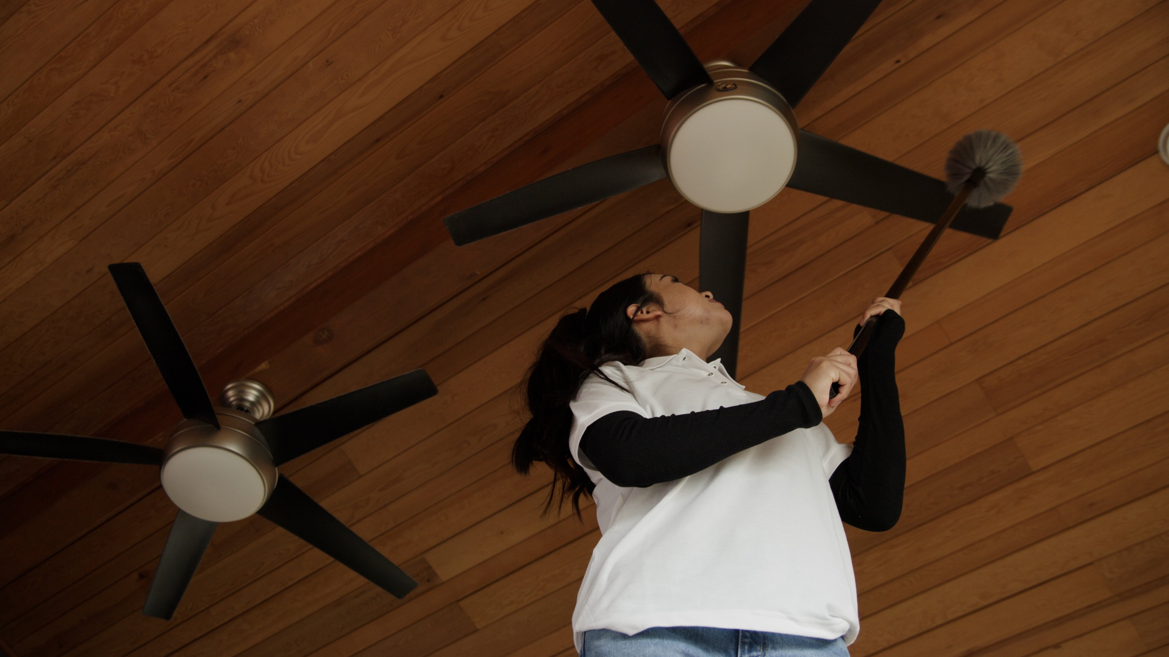 Woman cleans ceiling fan with duster